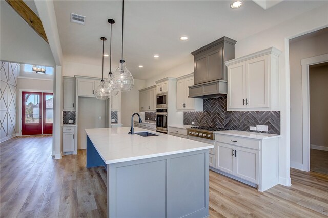 kitchen featuring visible vents, stainless steel appliances, a center island with sink, a sink, and light wood-type flooring