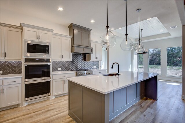 kitchen with a sink, custom range hood, appliances with stainless steel finishes, light wood-type flooring, and visible vents