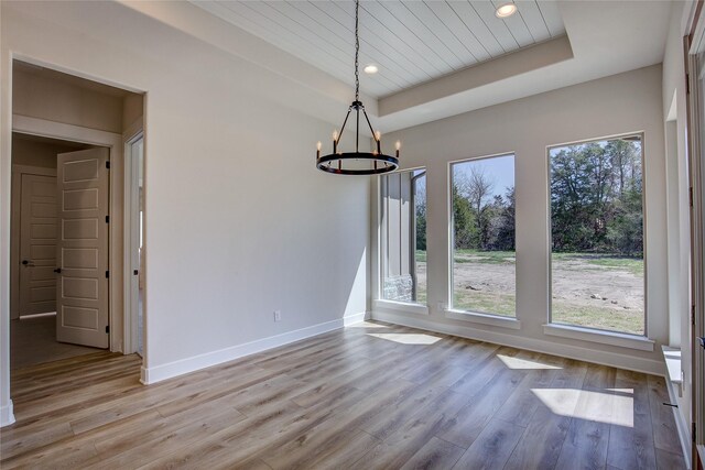 unfurnished dining area featuring a chandelier, baseboards, wood finished floors, recessed lighting, and a tray ceiling