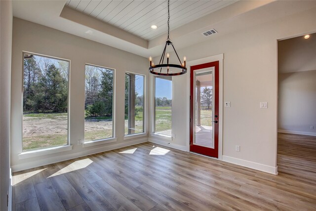 unfurnished dining area featuring a raised ceiling, a notable chandelier, wood finished floors, and visible vents