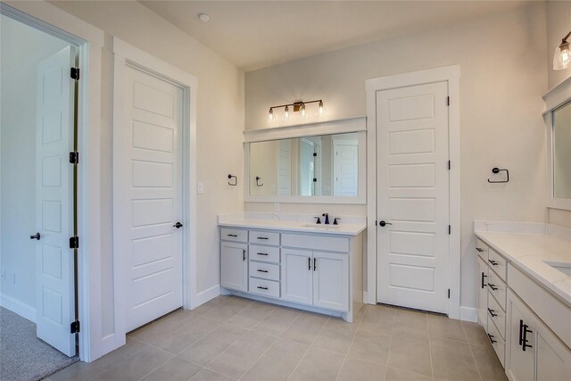 bathroom with baseboards, a sink, tile patterned flooring, and two vanities