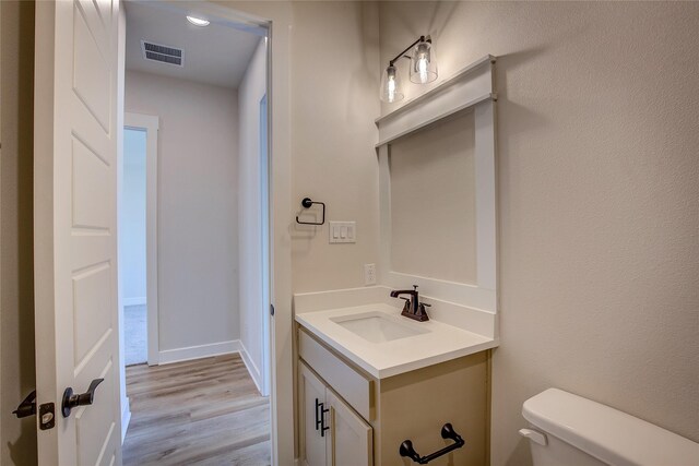half bath featuring vanity, toilet, baseboards, visible vents, and wood finished floors