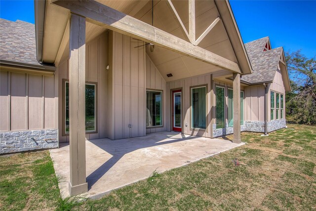 rear view of property with stone siding, a lawn, board and batten siding, and a patio area