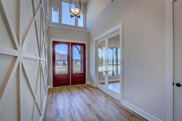 foyer featuring french doors, a towering ceiling, baseboards, and light wood-type flooring