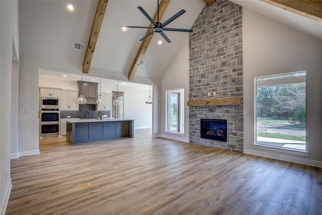 unfurnished living room with a ceiling fan, beamed ceiling, light wood-style flooring, and visible vents