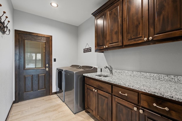clothes washing area with recessed lighting, a sink, washer and dryer, light wood finished floors, and cabinet space