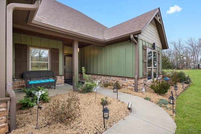 view of exterior entry with a porch, board and batten siding, a shingled roof, and stone siding