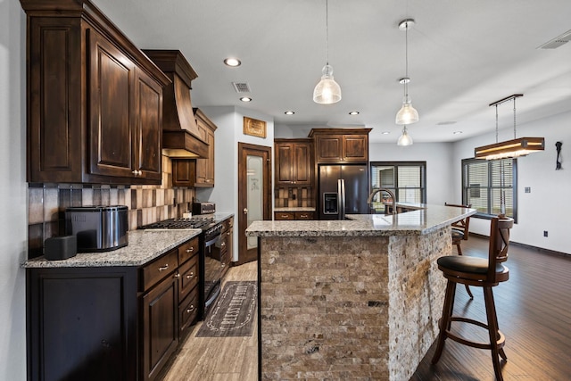 kitchen featuring fridge with ice dispenser, a kitchen breakfast bar, visible vents, range with gas cooktop, and wood finished floors