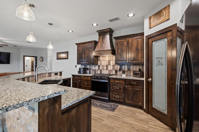 kitchen featuring visible vents, a sink, stainless steel gas range, premium range hood, and light stone countertops