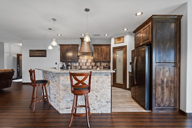 kitchen with black fridge, dark brown cabinets, recessed lighting, a center island with sink, and backsplash