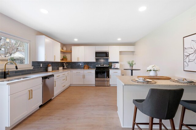 kitchen with a sink, backsplash, light countertops, appliances with stainless steel finishes, and open shelves