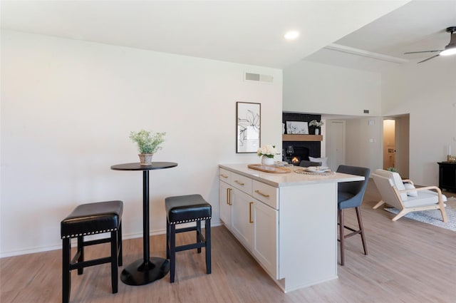 kitchen with visible vents, open floor plan, a kitchen bar, a warm lit fireplace, and white cabinets