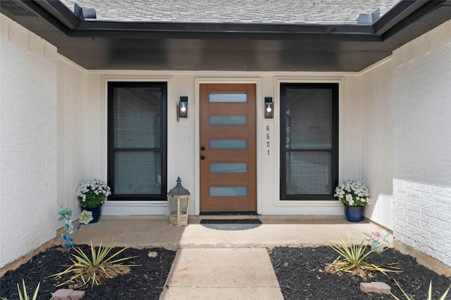 property entrance featuring brick siding and roof with shingles