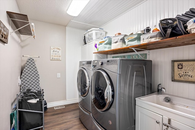 laundry area featuring visible vents, dark wood finished floors, cabinet space, a textured ceiling, and washer and clothes dryer