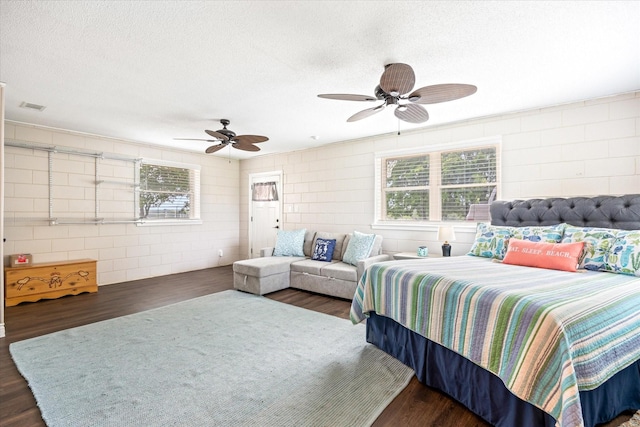 bedroom featuring visible vents, a textured ceiling, concrete block wall, and wood finished floors