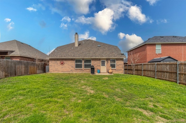 rear view of property featuring a lawn, a fenced backyard, brick siding, and a chimney