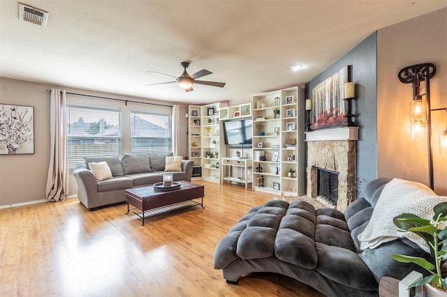 living area with ceiling fan, a fireplace, baseboards, wood finished floors, and visible vents