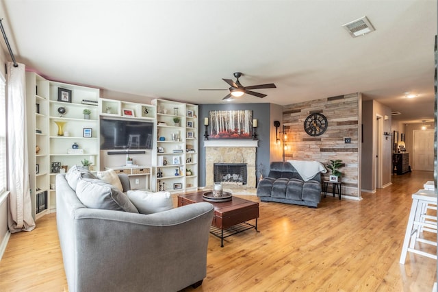 living room featuring visible vents, a ceiling fan, a fireplace, and light wood-type flooring