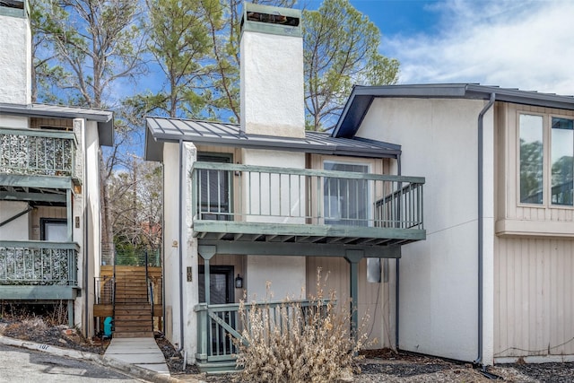 back of house featuring stucco siding, a balcony, and a chimney
