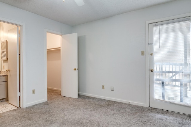 unfurnished bedroom featuring a walk in closet, baseboards, light colored carpet, ensuite bathroom, and a closet