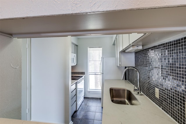 kitchen with white appliances, a sink, white cabinetry, dark tile patterned floors, and tasteful backsplash