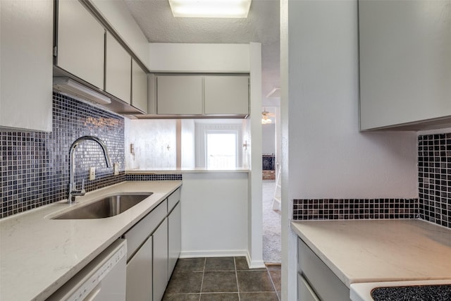 kitchen featuring backsplash, dark tile patterned floors, white dishwasher, a textured ceiling, and a sink