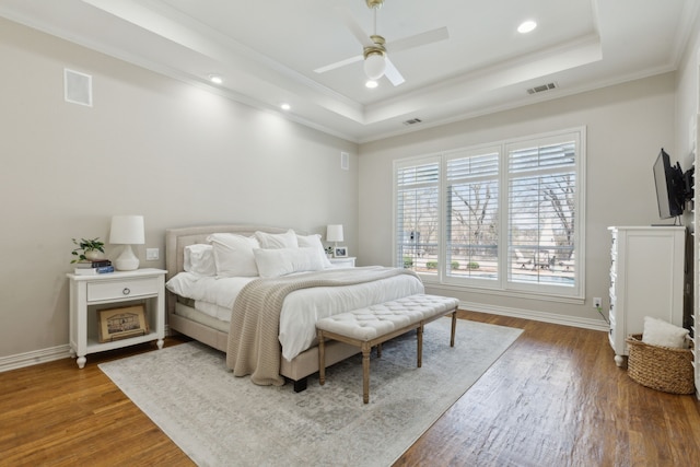 bedroom featuring visible vents, crown molding, a raised ceiling, and wood finished floors