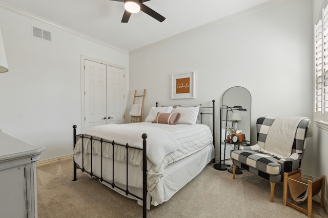 bedroom with visible vents, light colored carpet, ornamental molding, a closet, and a ceiling fan