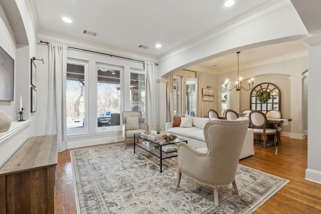 living room with visible vents, crown molding, an inviting chandelier, wood finished floors, and arched walkways