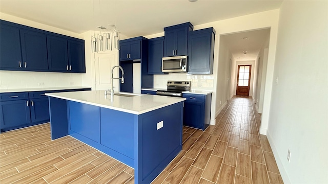 kitchen with wood finish floors, appliances with stainless steel finishes, blue cabinets, and a sink