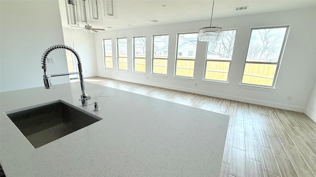 interior space featuring a sink, visible vents, baseboards, light wood-style floors, and decorative light fixtures