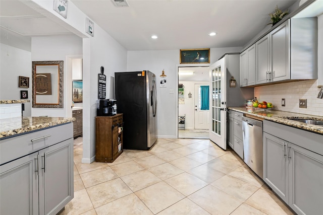 kitchen with light stone countertops, gray cabinets, a sink, decorative backsplash, and stainless steel appliances