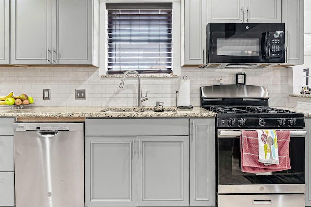 kitchen featuring backsplash, light stone countertops, appliances with stainless steel finishes, and a sink