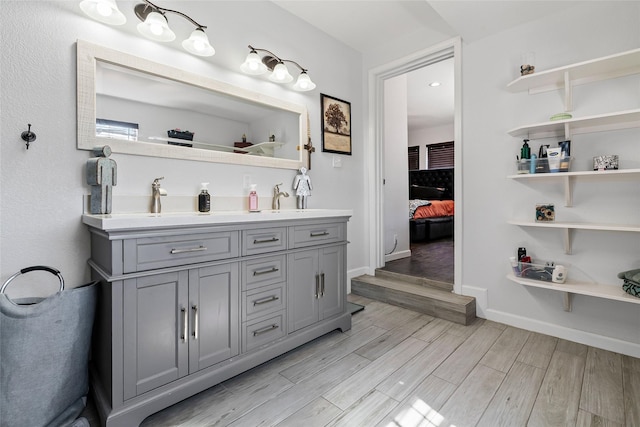 ensuite bathroom featuring wood finished floors, baseboards, double vanity, a sink, and connected bathroom