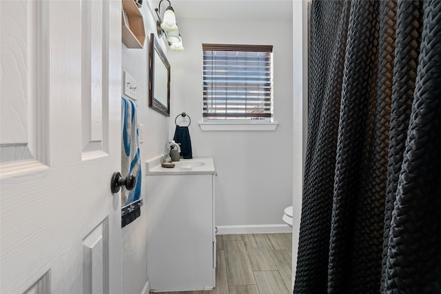 bathroom featuring wood finish floors, baseboards, toilet, and vanity