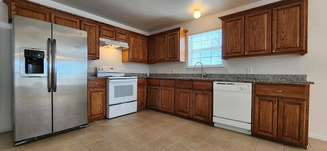 kitchen with under cabinet range hood, a sink, dark stone counters, white appliances, and light tile patterned floors