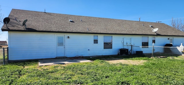 back of house with a lawn, a patio, central AC, fence, and roof with shingles