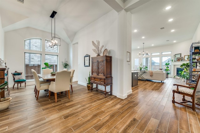 dining room featuring high vaulted ceiling, a fireplace, recessed lighting, a notable chandelier, and light wood-type flooring
