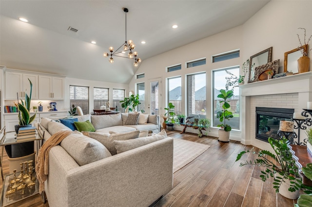 living room with light wood finished floors, visible vents, a brick fireplace, a chandelier, and high vaulted ceiling