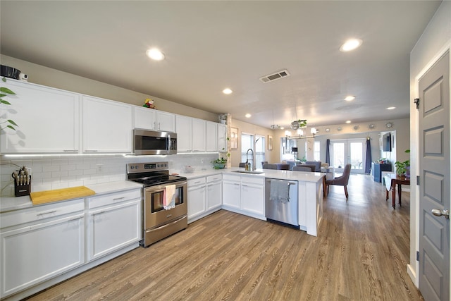 kitchen featuring visible vents, open floor plan, appliances with stainless steel finishes, a peninsula, and a sink