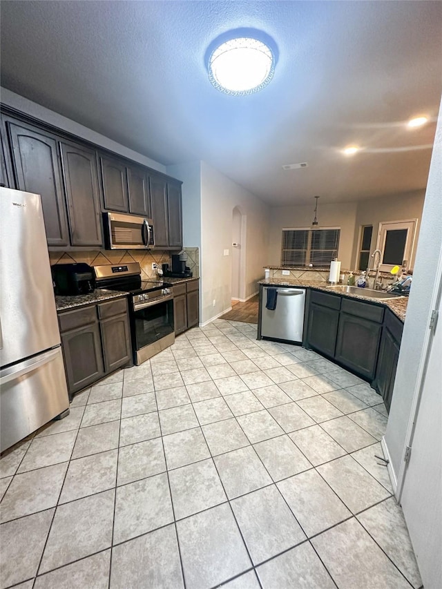 kitchen featuring tasteful backsplash, dark stone countertops, stainless steel appliances, and a sink