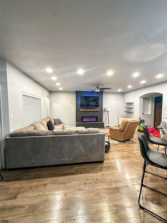 living room featuring a ceiling fan, recessed lighting, arched walkways, a textured ceiling, and light wood-type flooring