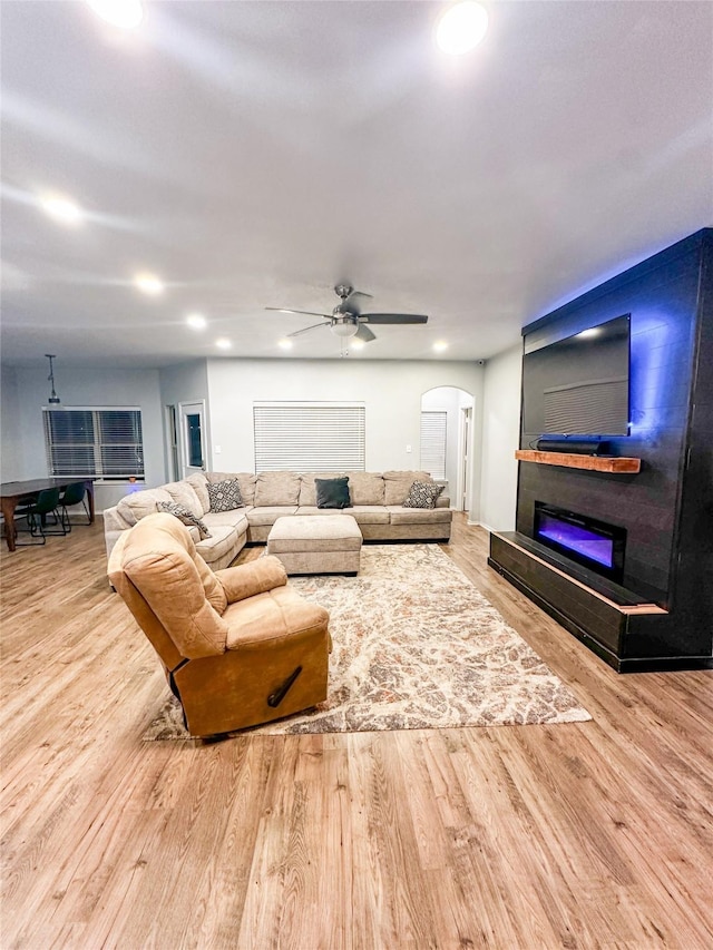 living room featuring ceiling fan, recessed lighting, wood finished floors, arched walkways, and a glass covered fireplace