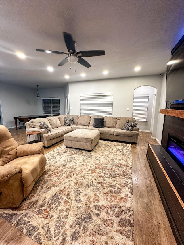 living area featuring ceiling fan, light wood-type flooring, arched walkways, a glass covered fireplace, and a textured ceiling