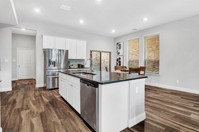 kitchen featuring appliances with stainless steel finishes, a sink, dark countertops, baseboards, and dark wood-style floors