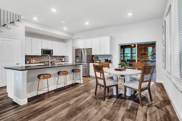 kitchen with tasteful backsplash, appliances with stainless steel finishes, a sink, dark countertops, and dark wood-style floors