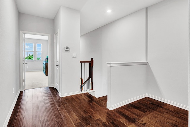 corridor featuring dark wood-type flooring, baseboards, and an upstairs landing