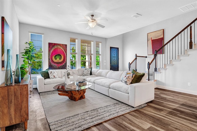 living area with visible vents, a ceiling fan, wood finished floors, and stairs