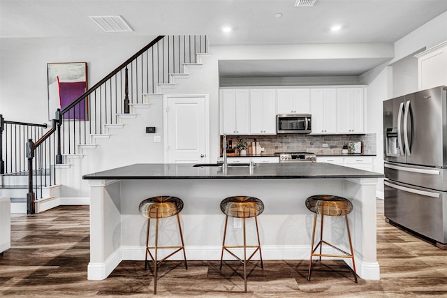 kitchen featuring a breakfast bar, appliances with stainless steel finishes, a sink, dark countertops, and dark wood-style floors
