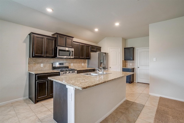 kitchen featuring a kitchen island with sink, a sink, tasteful backsplash, stainless steel appliances, and dark brown cabinetry